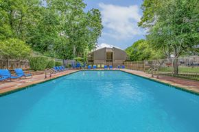 Plano apartment for rent - A large swimming pool surrounded by trees and blue lounge chairs.