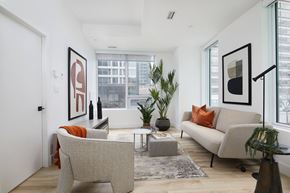 Montreal apartment for rent - A living room with a grey couch, a grey chair, a coffee table, and a large window.