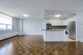 Toronto apartment for rent - A kitchen with a refrigerator, stove, and cabinets is visible from a living room.