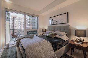 Toronto apartment for rent - A bedroom with a large bed and a city view through the window.