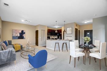 A living room with a couch a table and a chair and a kitchen in the background