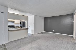 Titusville apartment for rent - the living room and kitchen of an apartment with a gray carpet and white walls at Windover Oaks Apartments, Titusville, FL