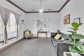 Ft Worth apartment for rent - A living room with a grey couch, a yellow pillow, a grey armchair, a wooden side table, a white wall with pictures and a plant.