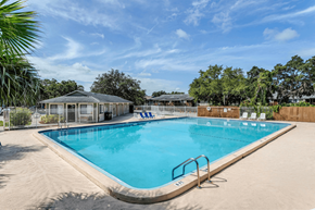 Titusville apartment for rent - A large outdoor swimming pool surrounded by a sandy area and trees at Windover Oaks Apartments, Florida