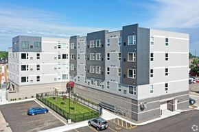 Owatonna apartment for rent - A modern multi-story building with a parking lot in front.