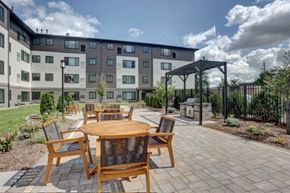 Rochester apartment for rent - A patio with a table and chairs is surrounded by a grassy area and a building.