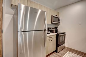 Rochester apartment for rent - A stainless steel refrigerator stands in a kitchen with wooden cabinets and a microwave above the stove.