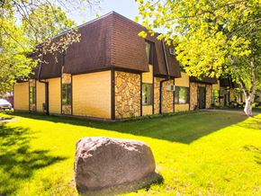 Little Falls apartment for rent - A large rock sits in the foreground of a building with a brown roof and yellow walls.