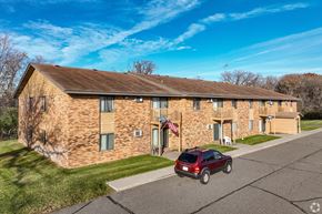 Elk River apartment for rent - A brick building with a flag on the front and a red car parked in front.