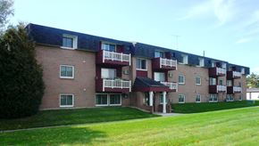 St Cloud apartment for rent - A red brick building with white balconies and a green lawn in front.