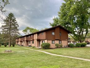 Greendale townhouse for rent - A long building with a brown roof and windows is surrounded by trees and grass at Root River Apartments, Greendale, WI, 53129