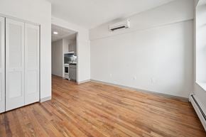 Worcester apartment for rent - A room with wooden floors and a white wall with a small kitchen in the background.