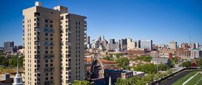 Baltimore apartment for rent - A tall building with many windows is in the foreground of a cityscape.