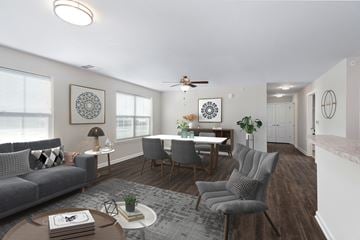 Baltimore apartment for rent - A living room with a grey sofa, a grey armchair, a wooden coffee table, a round table with chairs, a ceiling fan, and a rug.