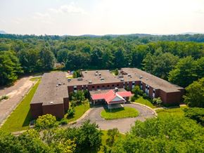 Northampton apartment for rent - A large red building surrounded by trees and a parking lot.