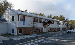 East Wareham apartment for rent - A building with a red brick wall and a white siding with a car parked in front.