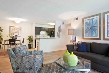 Douglasville apartment for rent - A living room with a grey couch, a patterned armchair, and a glass coffee table with a green vase on it.