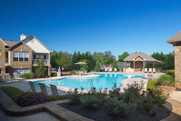 Mcdonough apartment for rent - A large swimming pool surrounded by a brick patio and a small garden.