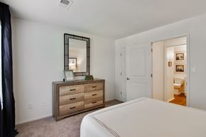 Stone Mountain apartment for rent - A bedroom with a large bed, a dresser with a mirror, and a door leading to another room.