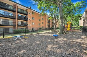 Alexandria apartment for rent - A playground area with a slide, swings, and a tree in front of a brick apartment building.