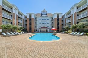 Largo apartment for rent - A large swimming pool surrounded by a brick patio and lounge chairs in front of apartment buildings.