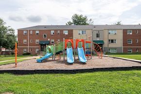 Hyattsville apartment for rent - A playground with a green slide and orange safety barriers in front of a brick building.