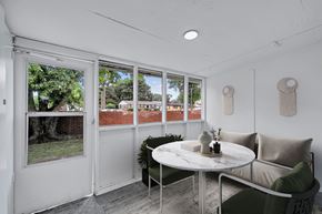 Hampton apartment for rent - A white table with a vase and a plant on it sits in front of a window with a view of a red fence and trees.