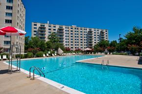 Bladensburg apartment for rent - A swimming pool with a red umbrella and a building in the background.