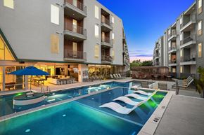 Austin apartment for rent - a resort style pool with lounge chairs in front of an apartment building