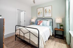 Gallatin apartment for rent - A bedroom with a black metal frame bed, a white comforter, and a small wooden table with a lamp on it.