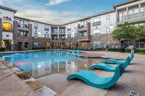 Grand Prairie apartment for rent - A swimming pool with a blue bench in front of a building.