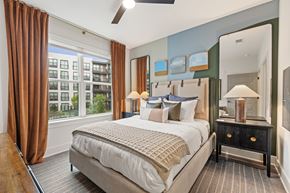 Chamblee apartment for rent - A bedroom with a large bed and a view of a building outside the window.