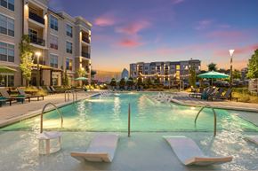 Buford apartment for rent - A large outdoor pool with sun loungers and a view of a city skyline at dusk.