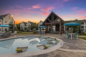 Cumming apartment for rent - A pool with a waterfall and a water slide in the middle of a patio with chairs and umbrellas.
