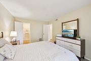 Bradenton apartment for rent - A bedroom with a large bed, a dresser with a mirror, and a lamp on a nightstand. at Sarasota South Apartments, Bradenton, FL