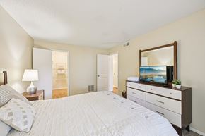 Bradenton apartment for rent - A bedroom with a large bed, a dresser with a mirror, and a lamp on a nightstand.