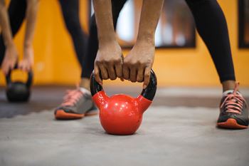 A person is holding a red kettlebell in a gym.