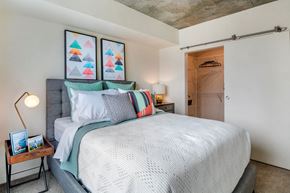 Tacoma apartment for rent - A bedroom with a bed, pillows, a nightstand, and a wall-mounted light fixture.