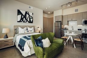 Austin apartment for rent - A modern bedroom with a green chair and a bed with a white comforter.