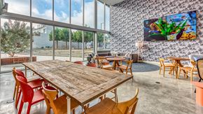 Los Angeles apartment for rent - A wooden table with red chairs is in the foreground of a room with a large TV mounted on the wall.