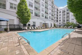Atlanta apartment for rent - A large swimming pool surrounded by a black fence and a white building in the background.