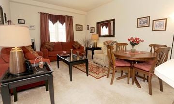 Exton apartment for rent - A living room with a brown sofa, a wooden dining table, and a red lamp.