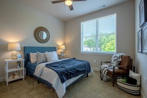 Webster Groves apartment for rent - A bedroom with a bed, chair, and ceiling fan at The Elle on Lockwood Apartments, Webster Groves, Missouri