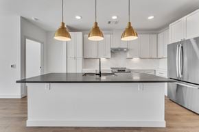Rogers apartment for rent - Kitchen island with dark countertop and brass pendant lights at Plaza at Pinnacle Hills Apartments, Rogers