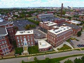 St Louis apartment for rent - A large brick building with a tall chimney is surrounded by other buildings and a parking lot.