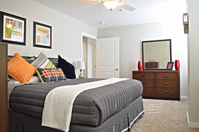 Saint Louis apartment for rent - bedroom with light carpeting, bed with gray duvet, brown dresser with mirror at Residences at Forest Park, Saint Louis, MO, 63108
