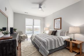 Chesterfield apartment for rent - model bedroom with plank flooring, ceiling fan, large windows, large bedroom with nightstand, accent chair and dresser at The Flats & Terraces at Wildhorse Village, Missouri
