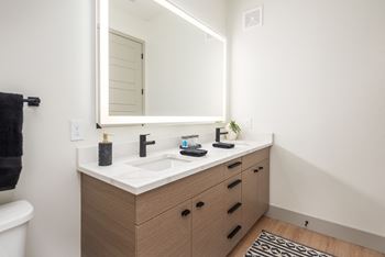 Bathroom vanity with modern wood cabinetry and backlit mirror