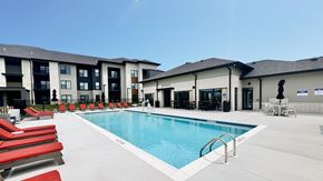 O’Fallon apartment for rent - A swimming pool with red lounge chairs and a building in the background.