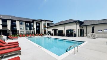 O’Fallon apartment for rent - A swimming pool with red lounge chairs and a building in the background.